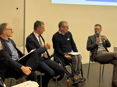 Podiumsdiskussion zwischen fünf Männern, davon einer im Rollstuhl, beim