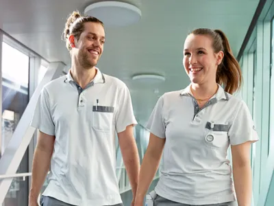 Zwei Pflegefachkräfte gehen zufrieden einen Spitalgang entlang. Paraplegie Juni 2025 Teaser