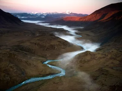 Ein leuchtend blauer Gletscherfluss schlängelt sich durch eine dunkle Landschaft.