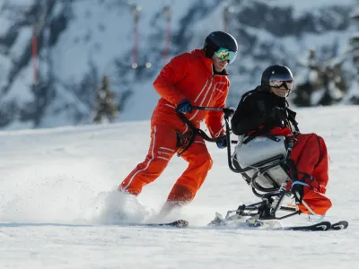 Monoskibob Fahrender wird von einem Skilehrer geführt.
