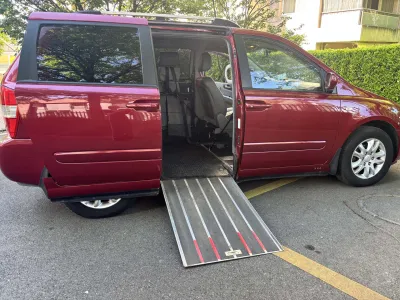 Roter Minivan mit offener Schiebetür und ausgefahrener Rollstuhlrampe auf einer Straße.