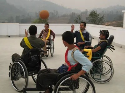 Indische Männer in Rollstühlen und mit gelben und roten Schärpen spielen mit einem Ball.