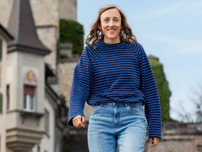 Smiling woman in blue sweater walking along street with historic building in background.