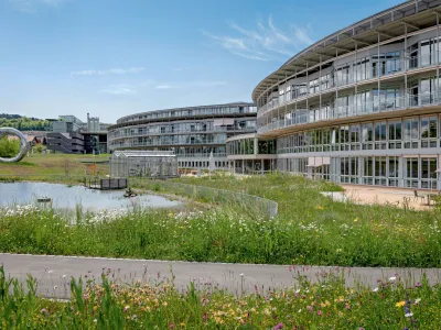Das moderne Gebäude mit viel Glas und Holzvertäfelung, umgeben von einer Rasenfläche und einem kleinen See.