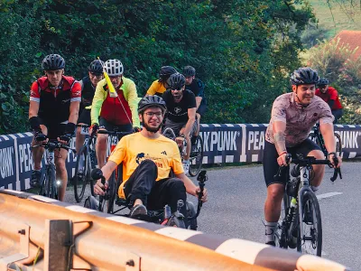 Ein Gruppe von Radfahrern auf einer Brücke in einen Park mit Bäumen im Hintergrund.