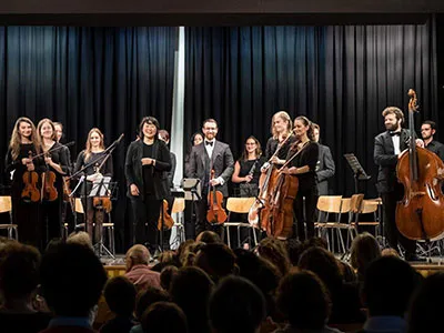 A symphony orchestra performing on stage with musicians playing various instruments, including violins, cellos, and other classical instruments.