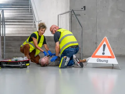 Zwei First Responder in Warnwesten versuchen, einer am Boden liegenden verletzten Person zu helfen.