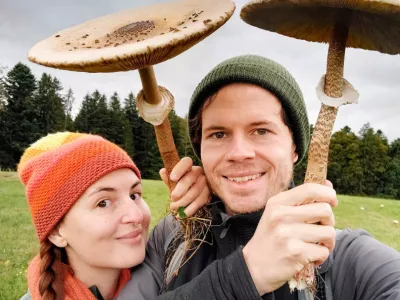 Two hikers standing under large mushroom-shaped umbrellas, smiling at the camera.