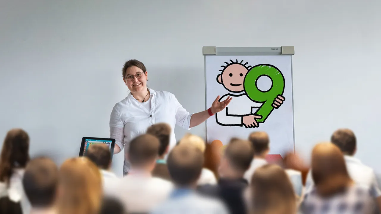 Susanna Präsentiert die Symbolsammlung Metacom 9 auf einer Flipchart. Viele Personen hören ihr dabei interessiert zu.