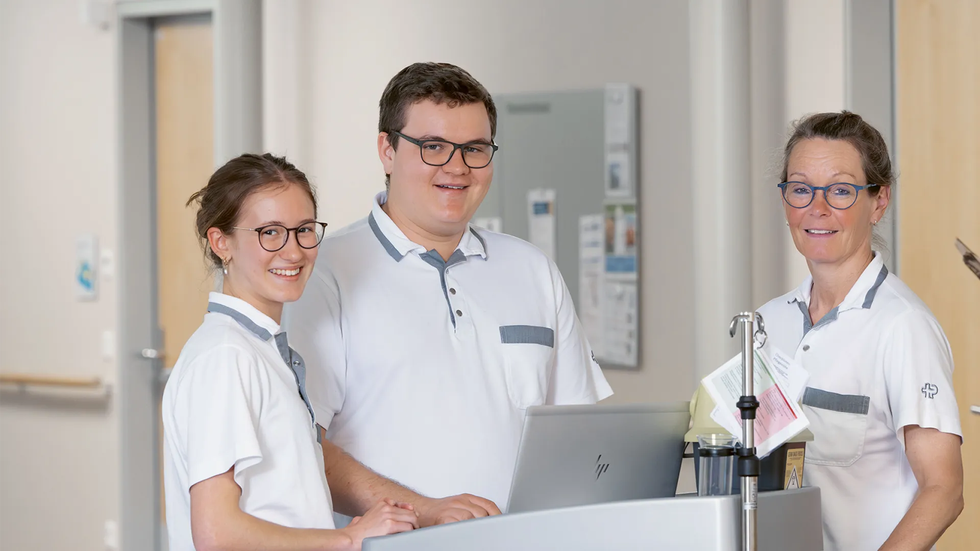 Drei Personen stehen um einen kleinen Tisch und lächeln in die Kamera