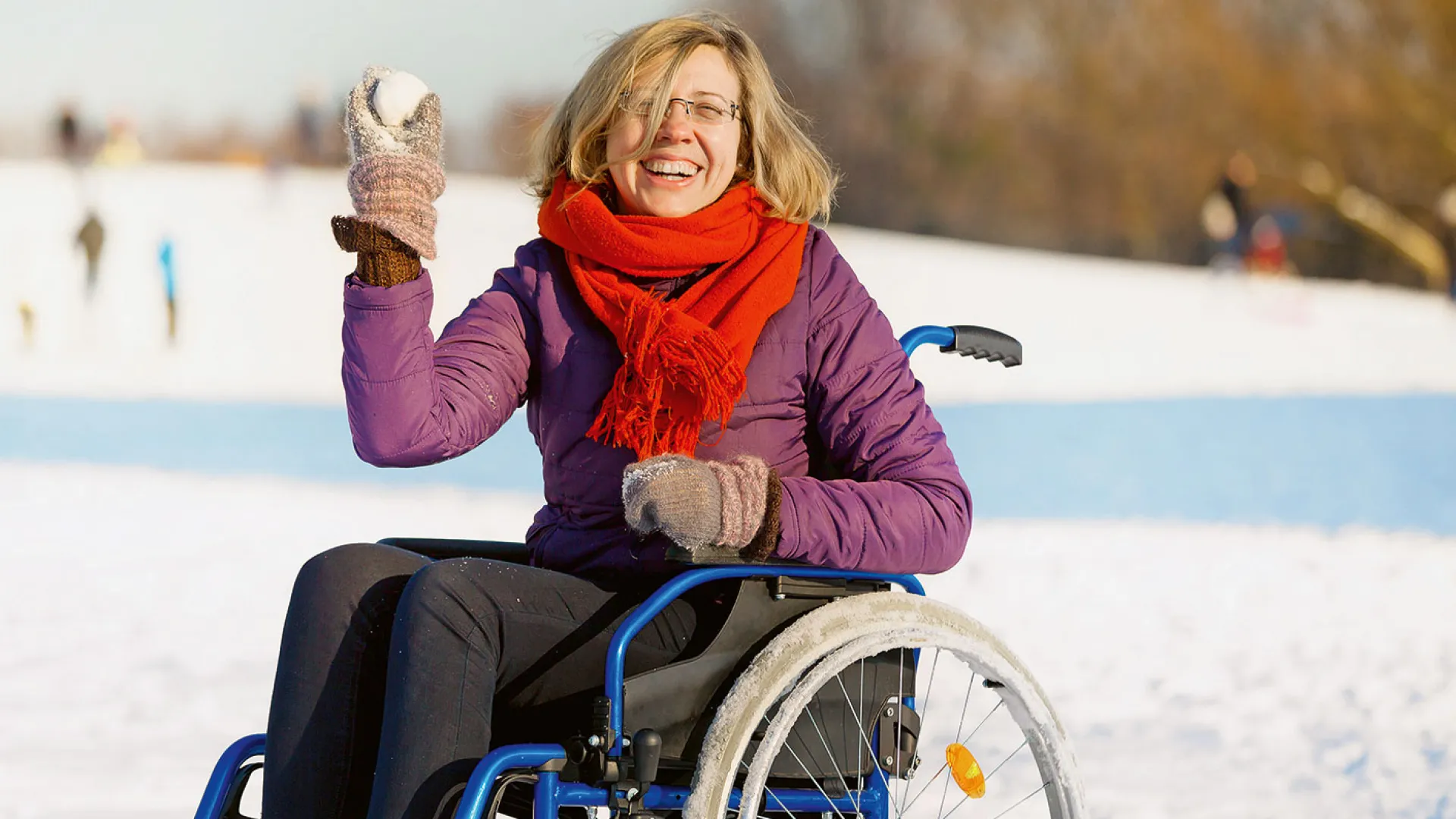 Lachende Frau sitzt im Rollstuhl und wirft einen Schneeball