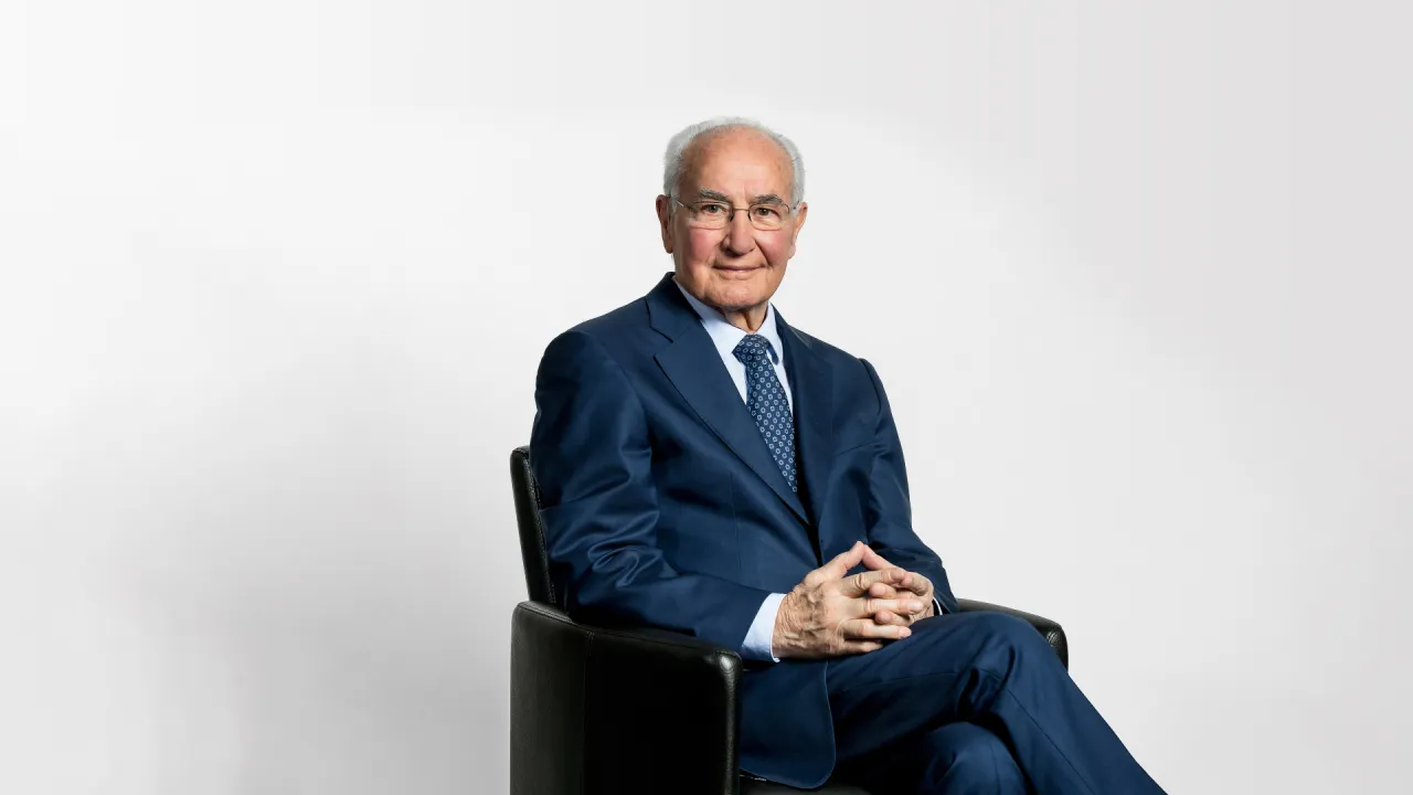 Guido A. Zäch in dunklem Anzug in einem Sessel.