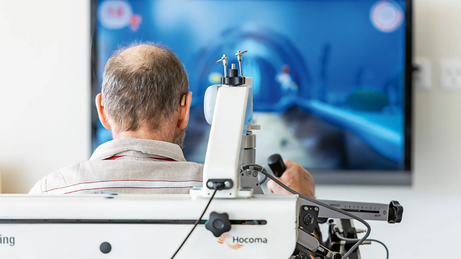 Ein Mann sitzt vor einem Bildschirm und übt mit einer Roboterhand.