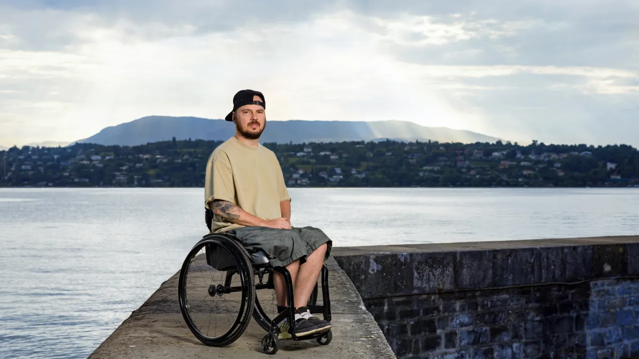 Anton Mityukov sitzt im Rollstuhl auf einem Steg aus Beton mit dem Genfersee im Hintergrund.