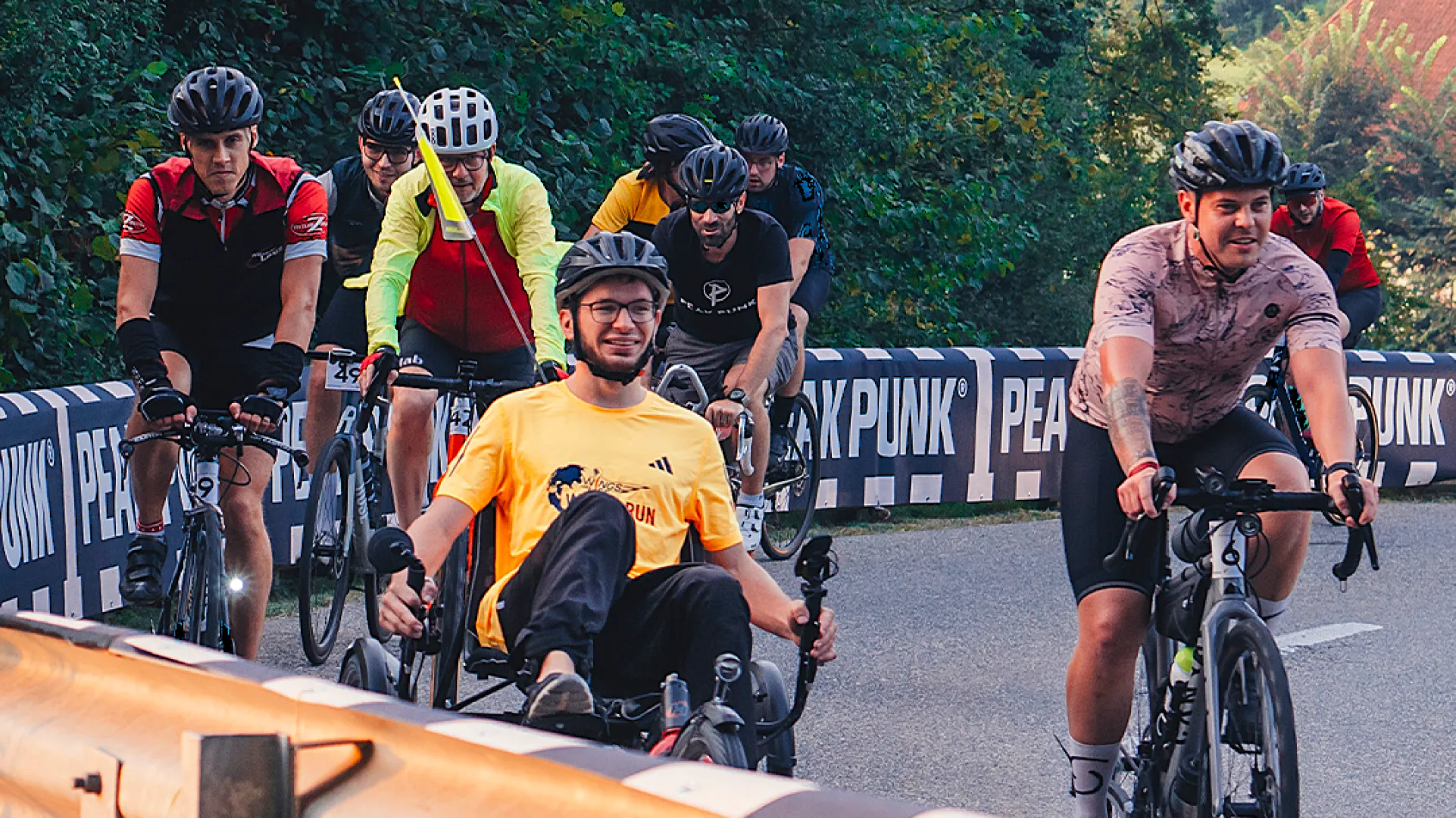 Ein Gruppe von Radfahrern auf einer Brücke in einen Park mit Bäumen im Hintergrund.