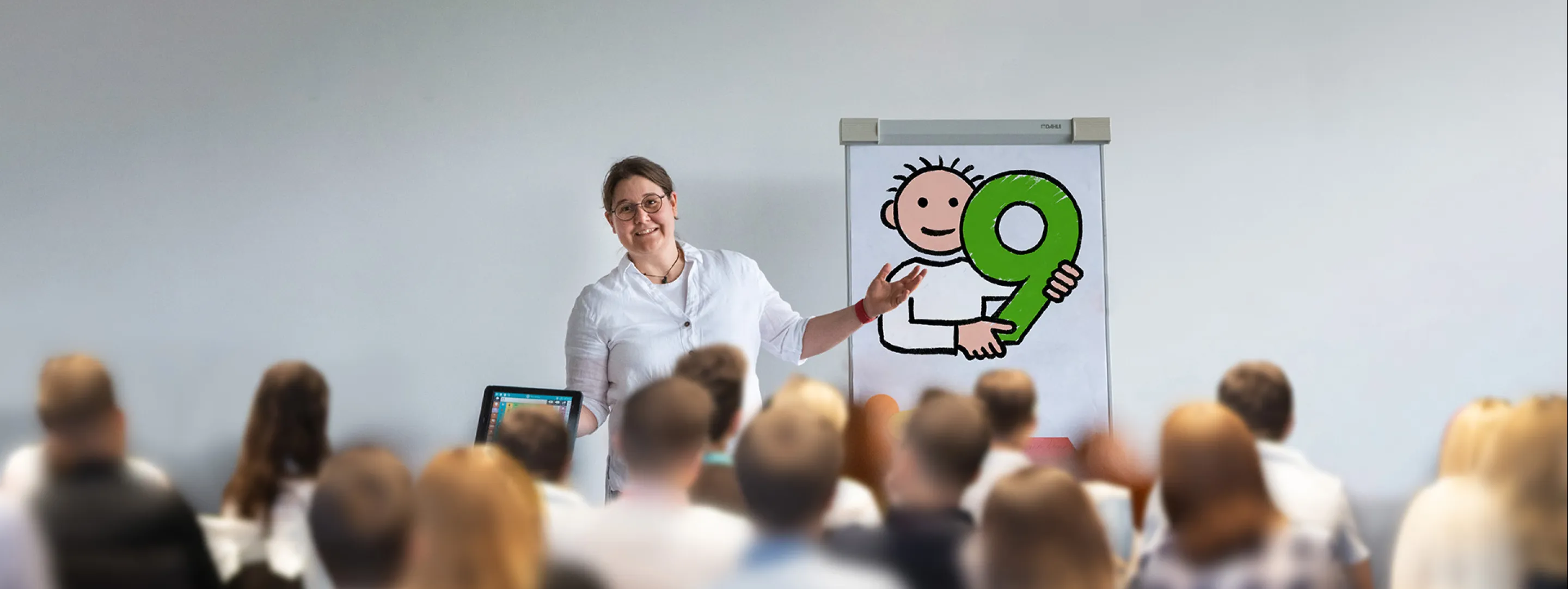 Susanna Präsentiert die Symbolsammlung Metacom 9 auf einer Flipchart. Viele Personen hören ihr dabei interessiert zu.