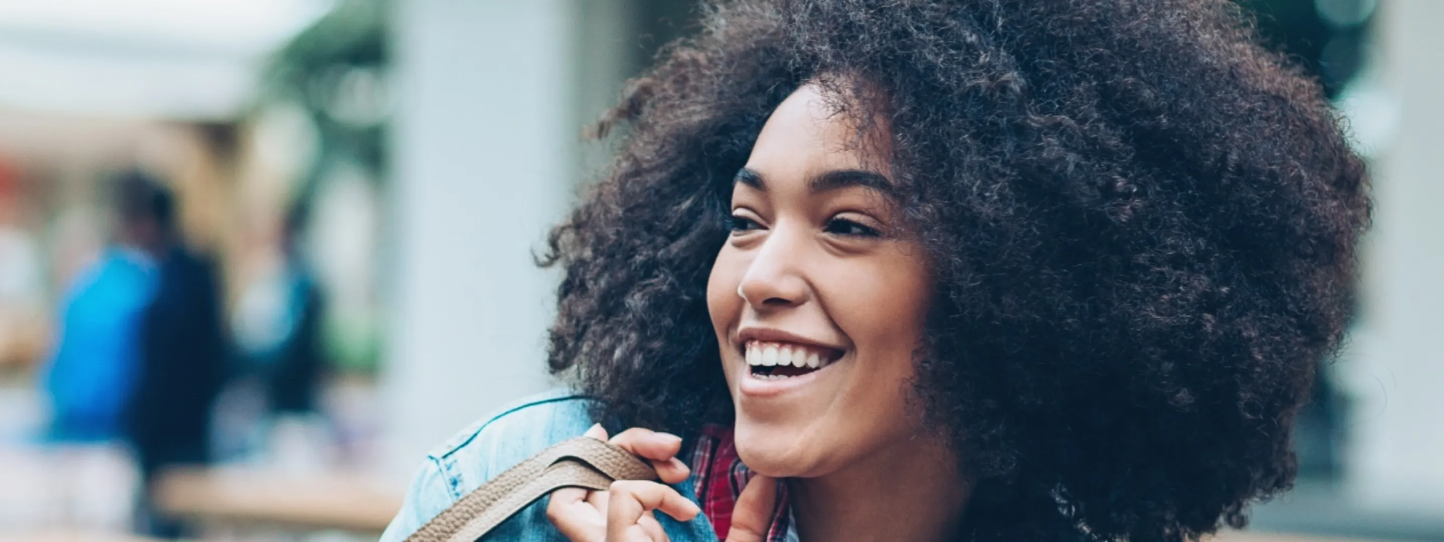 A woman is walking through the city, carrying her bag casually over her shoulder and laughing.