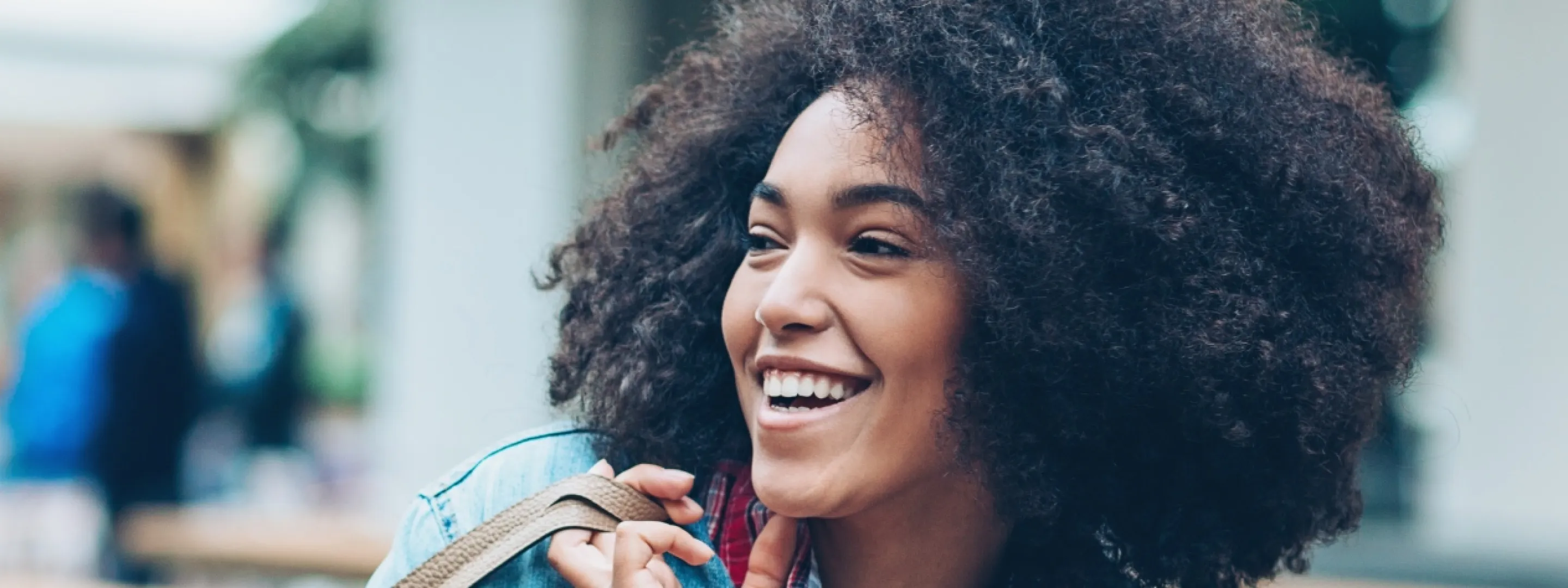 Une femme marche en ville, elle porte un sac à l’épaule et rit.
