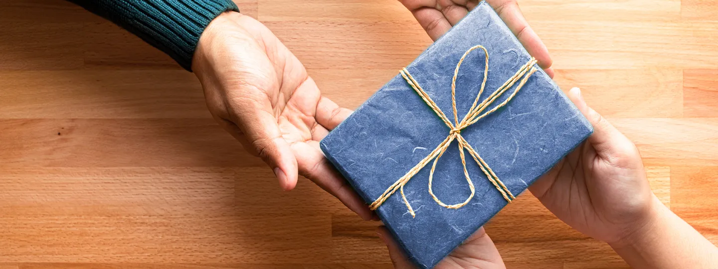 A man gives a child a gift wrapped in blue.