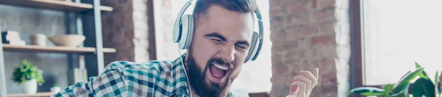 A man is wearing headphones, playing air guitar and singing.