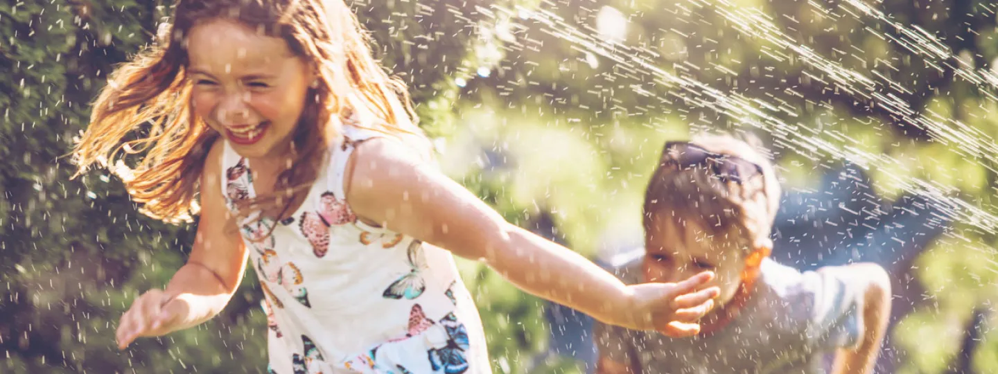 Kinder rennen durch den Rasensprinkler