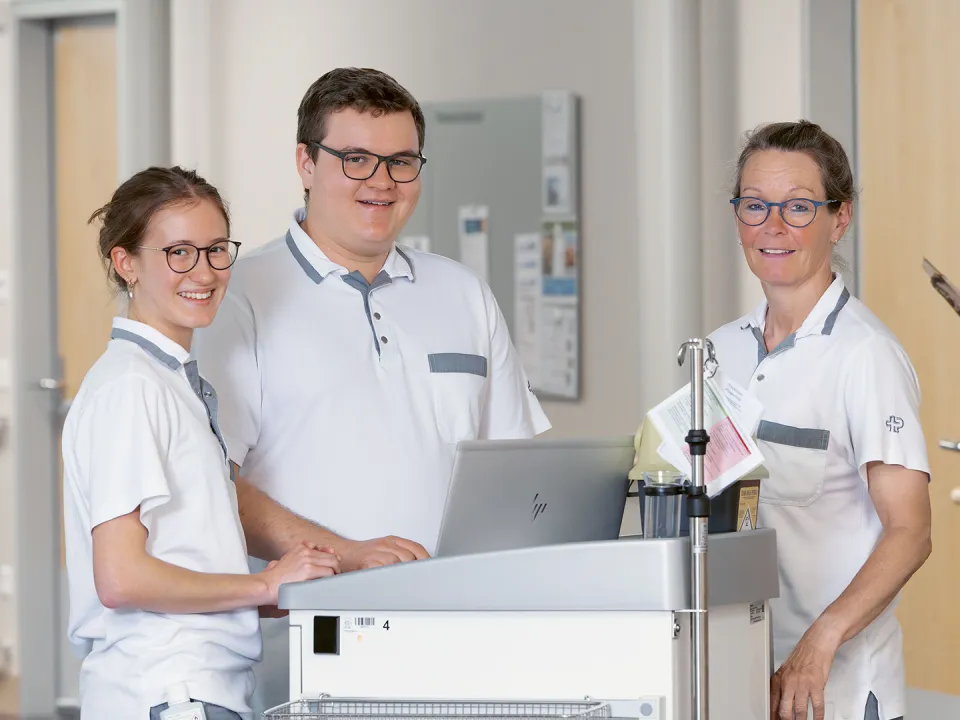 Drei Personen stehen um einen kleinen Tisch und lächeln in die Kamera