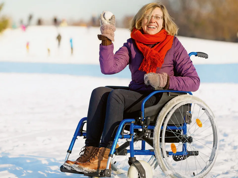 Lachende Frau sitzt im Rollstuhl und wirft einen Schneeball