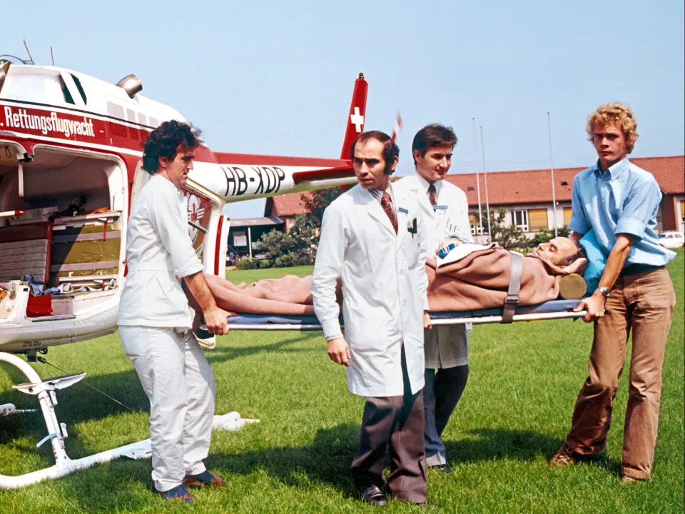 Guido A. Zäch und zwei weitere Männer transportieren einen Patienten aus dem Helikopter. Historisches Bild aus Basel.