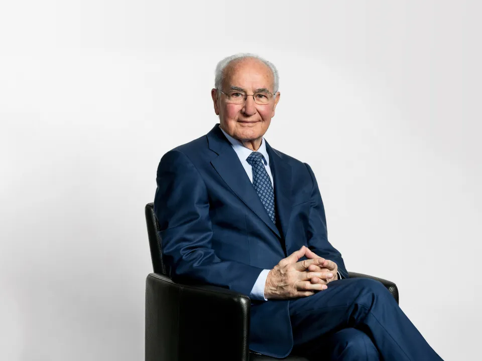 Guido A. Zäch in dunklem Anzug in einem Sessel.