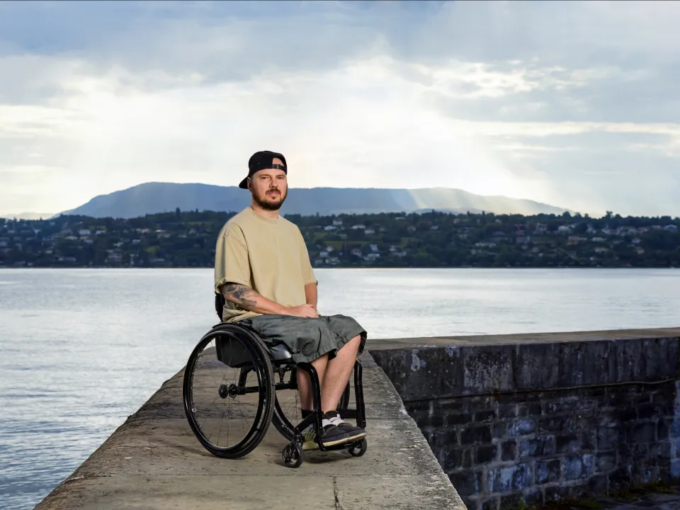 Anton Mityukov sitzt im Rollstuhl auf einem Steg aus Beton mit dem Genfersee im Hintergrund.