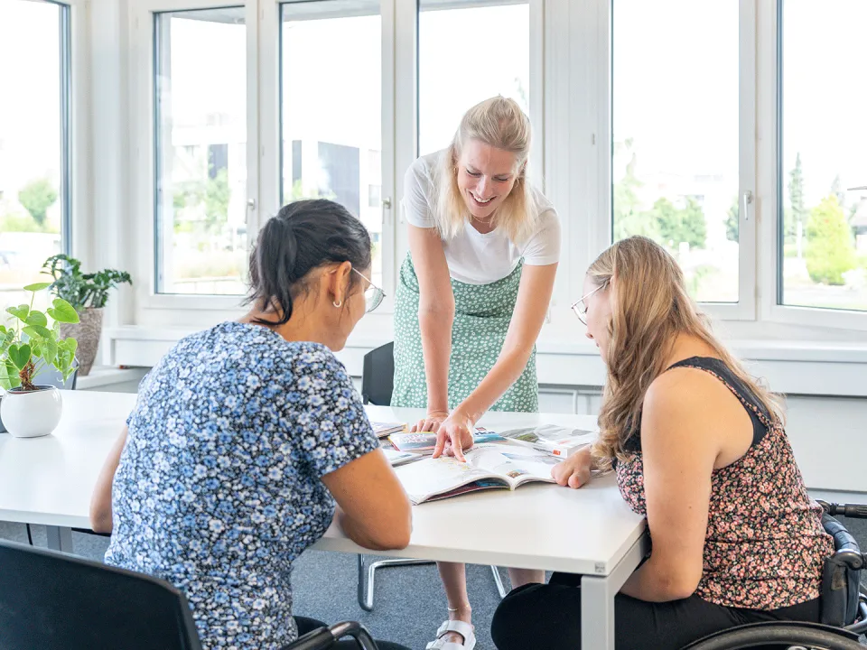 Drei Frauen sitzen um einen Tisch und besprechen etwas.