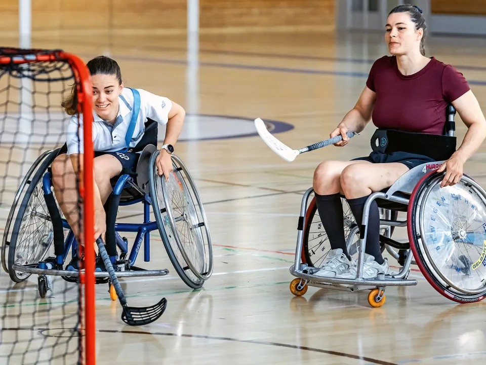 Zwei Frauen spielen Unihockey im Rollstuhl.