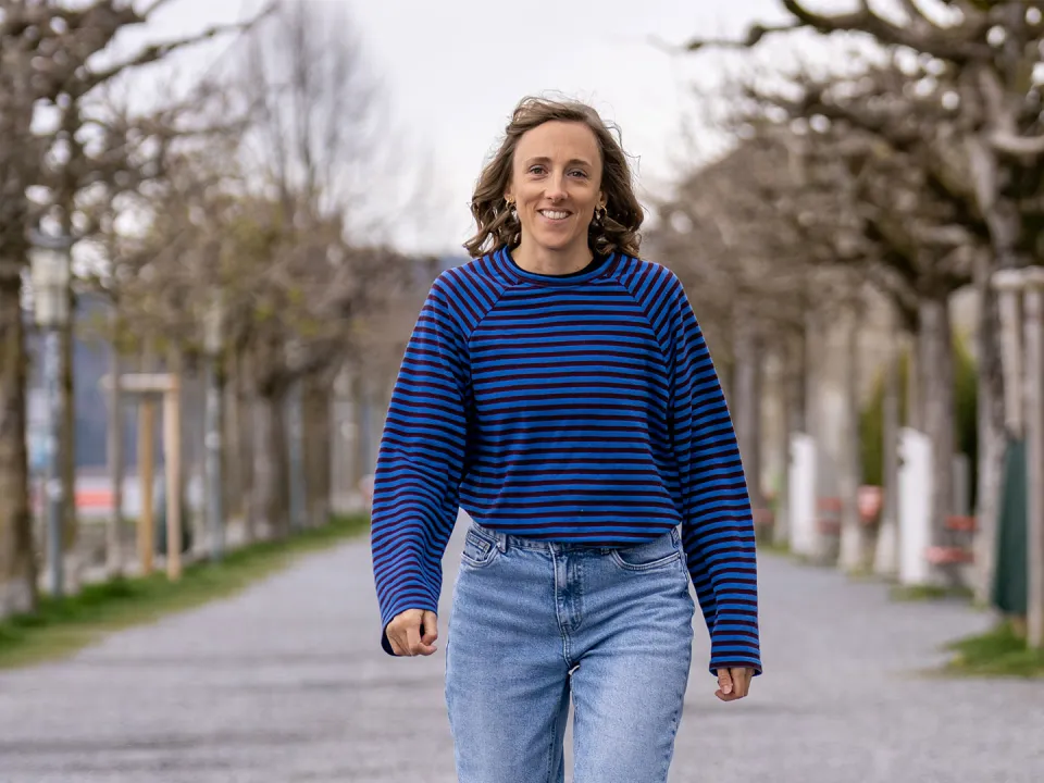 Woman in blue sweater walking along tree-lined path