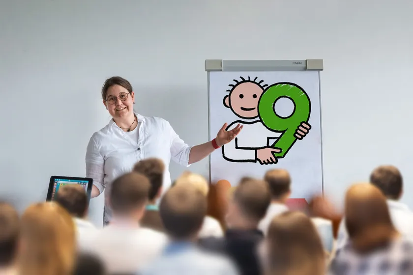 Susanna Präsentiert die Symbolsammlung Metacom 9 auf einer Flipchart. Viele Personen hören ihr dabei interessiert zu.