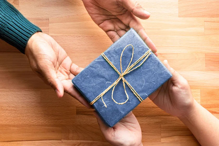 Ein Mann übergibt einem Kind ein blau eingepacktes Geschenk.