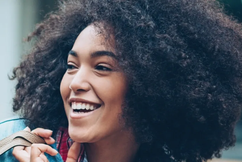 A woman is walking through the city, carrying her bag casually over her shoulder and laughing.