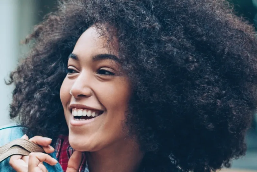 Une femme marche en ville, elle porte un sac à l’épaule et rit.