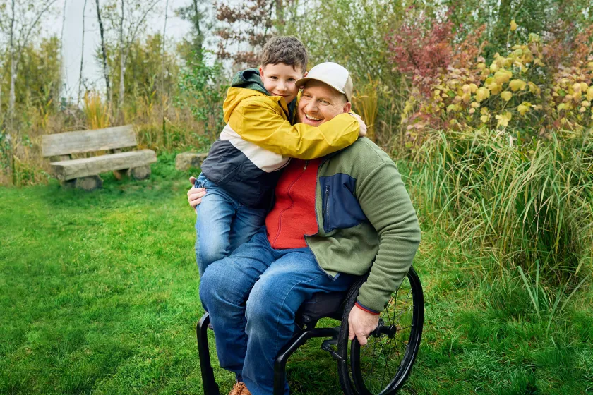Heiri siede nella sua carrozzina su un prato e suo figlio gli sale in grembo e abbraccia forte forte suo papà. Tutti e due sorridono.