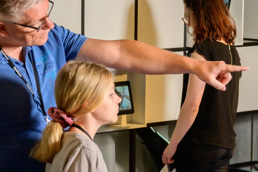 Eine Familie ist im Besuchszentrum ParaForum und schaut sich die Ausstellung an. Der Vater zeigt auf eine Wirbelsäule und seine Tochter hört ihm zu.