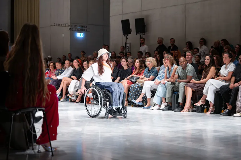Modeshow mit Rollstuhlfahrerin auf dem Laufsteg die inklusive Mode trägt.
