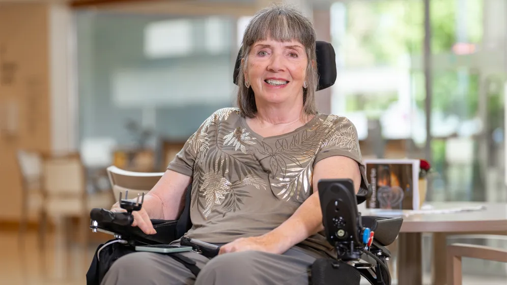 A smiling woman in a wheelchair in a room with a wooden interior.