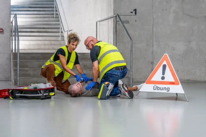 Zwei First Responder in Warnwesten versuchen, einer am Boden liegenden verletzten Person zu helfen.