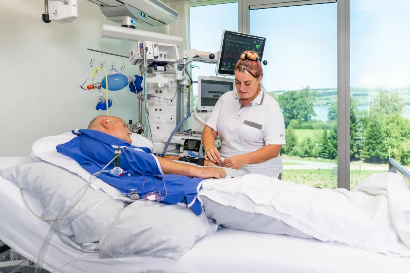 A nurse in hospital scrubs stands next to a patient's bed.