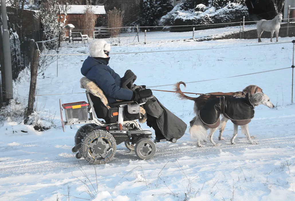 Elektrorollstuhl mit Schneeketten und Hundegespann fährt durch den Schnee