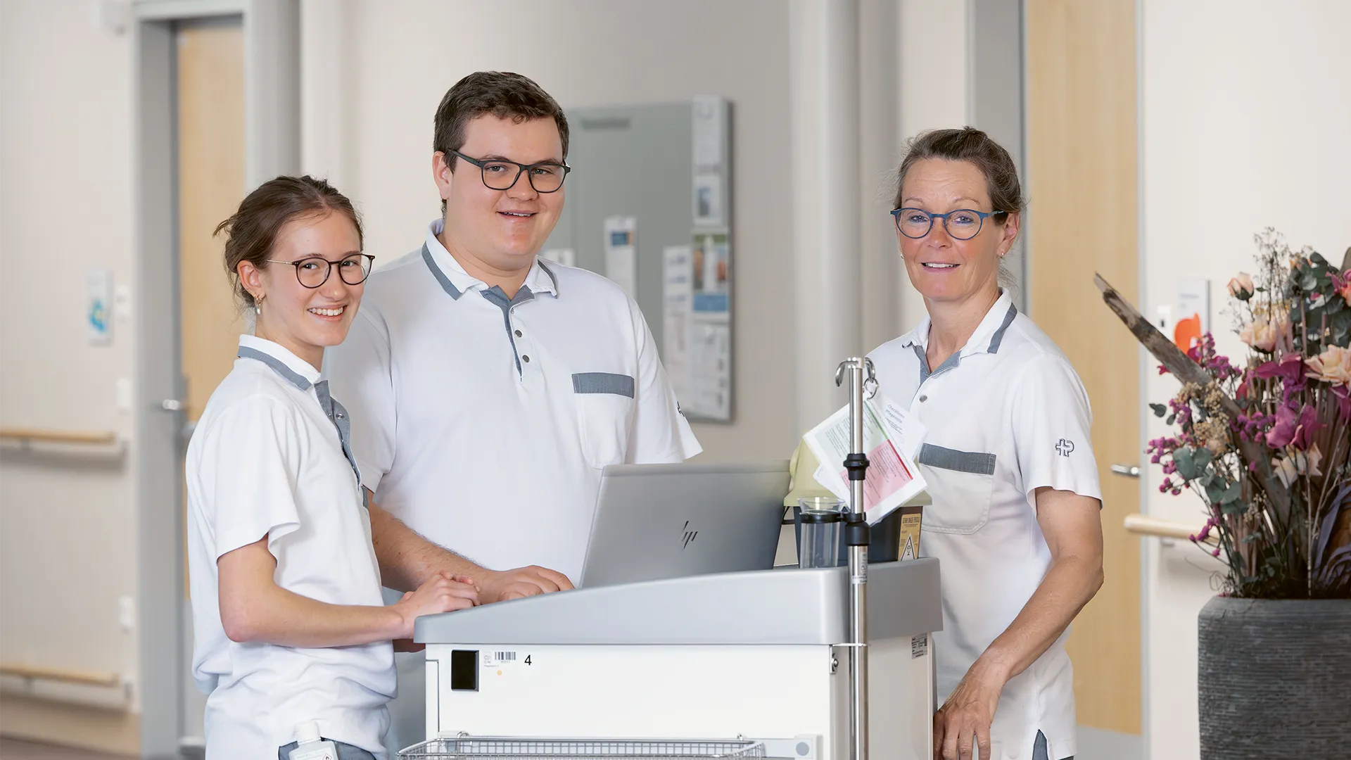 Drei Personen stehen um einen kleinen Tisch und lächeln in die Kamera