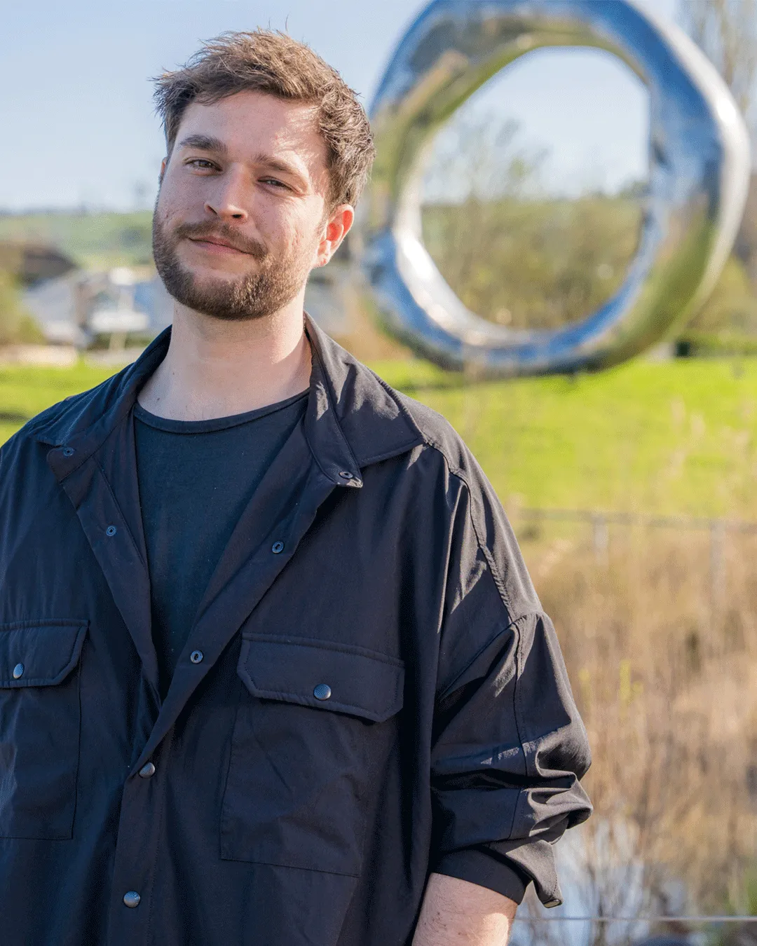 Zian steht vor dem Ring of Life auf dem Campus Nottwil und lächelt lässig in die Kamera. 