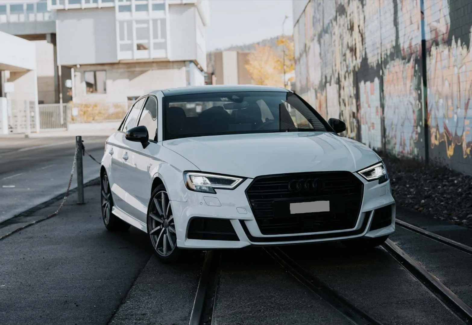 Weißer Audi A3 Sportback auf städtischer Straße vor Industriegebäude geparkt.