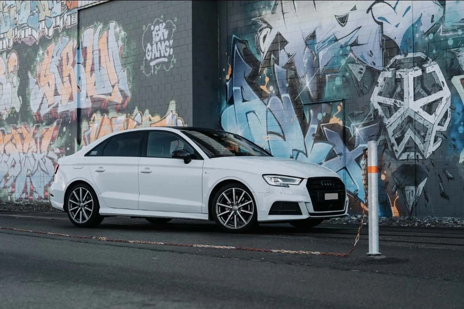 Weißer Audi-Sportwagen vor Wand mit buntem Graffiti geparkt.