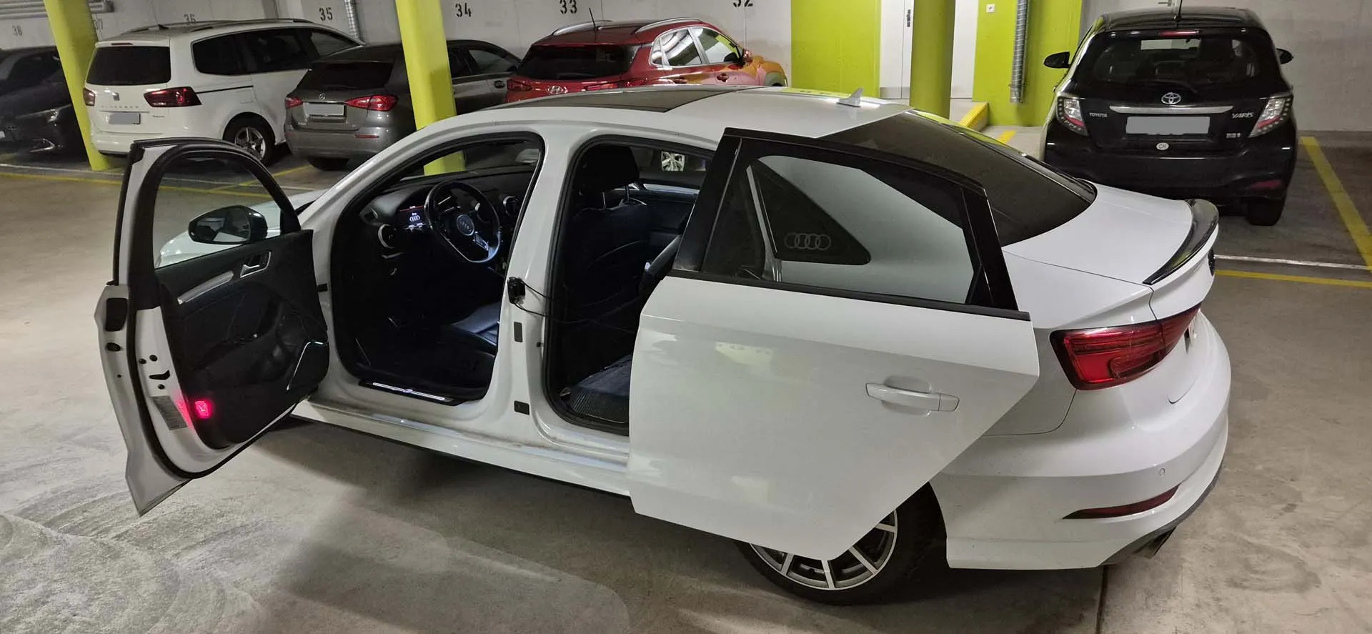 Roter Sportwagen mit geöffneten Türen in einer Tiefgarage. Innenraum in Weiß sichtbar.