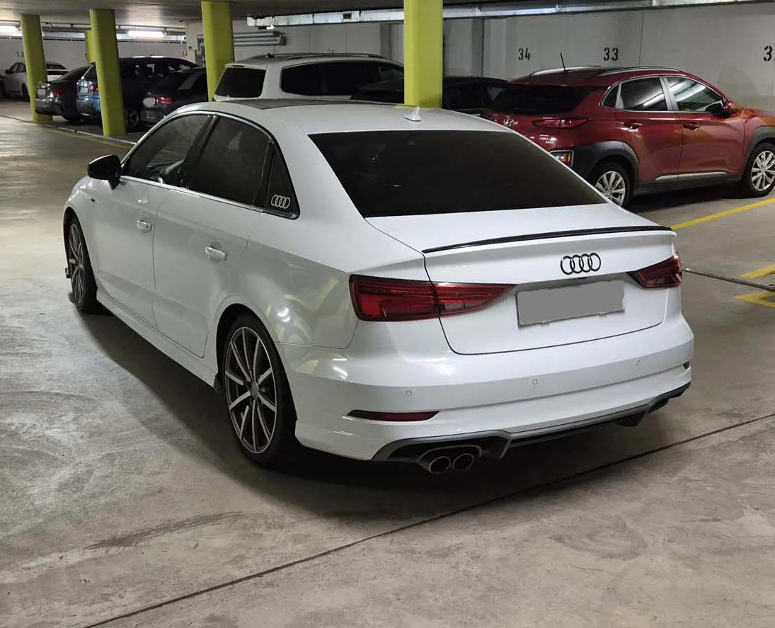 Weißer Audi A3 Limousine in einer Tiefgarage, neben anderen geparkten Autos.